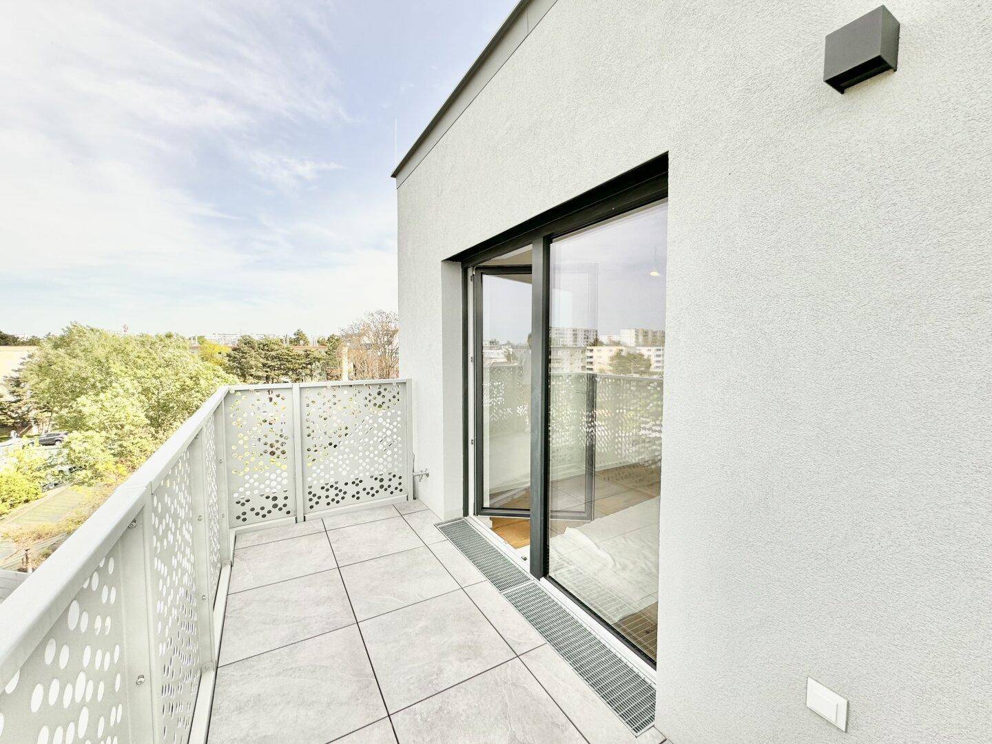 Heller Balkon mit Fliesenboden und großen Glastüren, die zu einem Innenraum führen.
