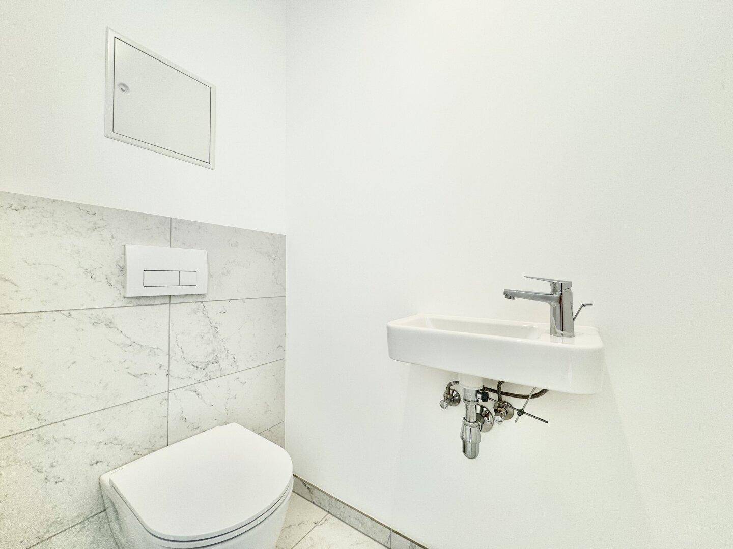 Modernes Gäste-WC mit wandhängender Toilette, kleinem Waschbecken und Marmorfliesen.