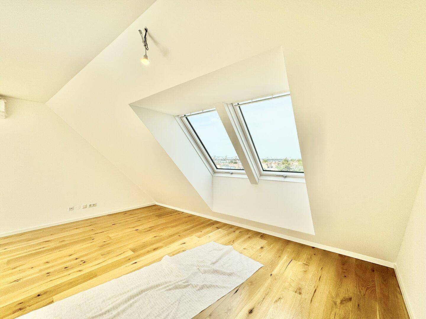 Heller Raum mit Holzboden, schräger Decke und zwei Dachfenstern für natürliches Licht.