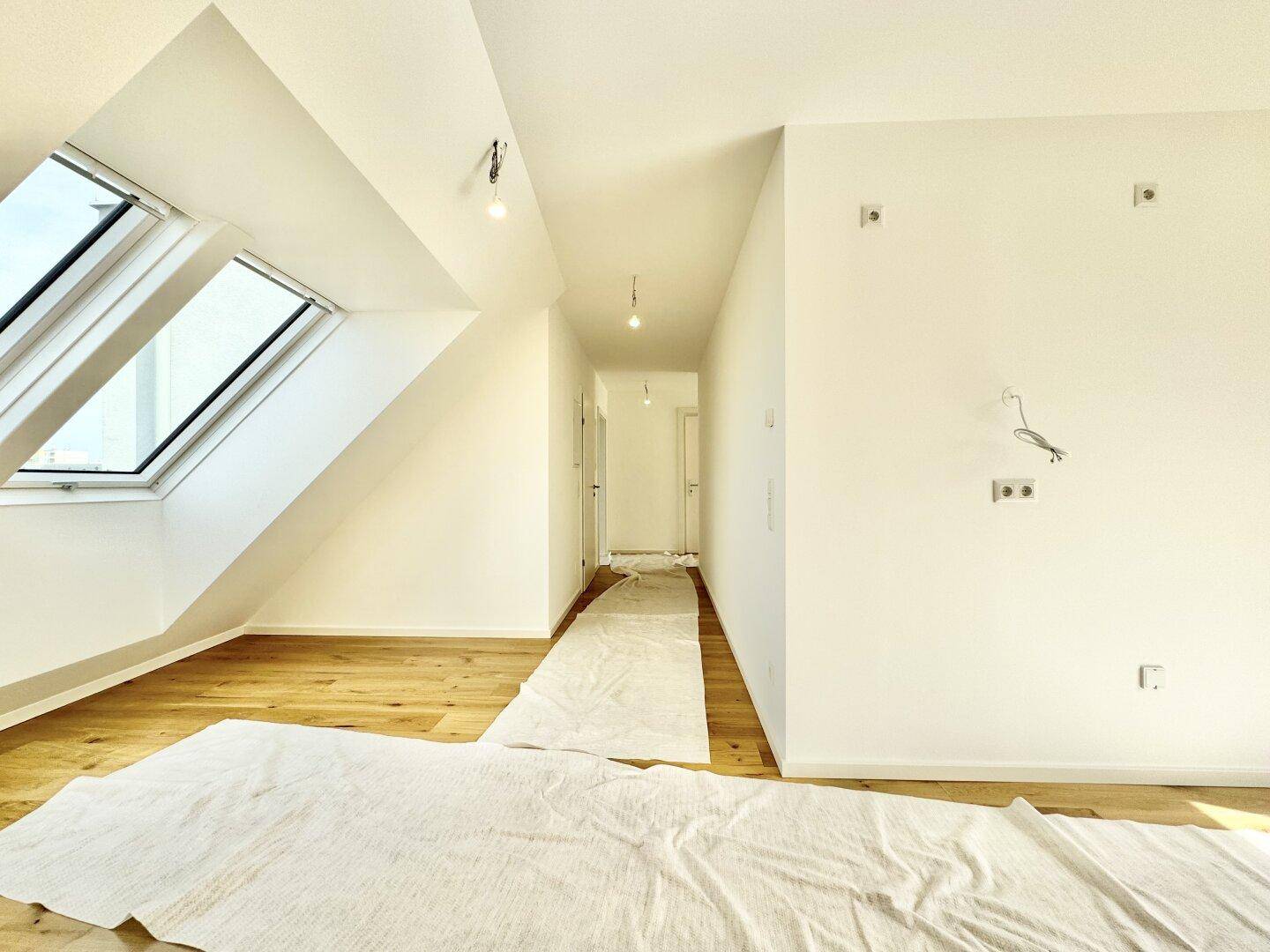 Heller Flur mit Holzboden, schräger Decke und Dachfenstern, führt zu weiteren Räumen.