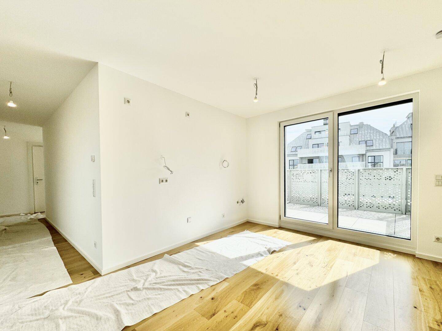Helles, unmöbliertes Wohnzimmer mit Holzboden und großen Schiebetüren zur Terrasse.