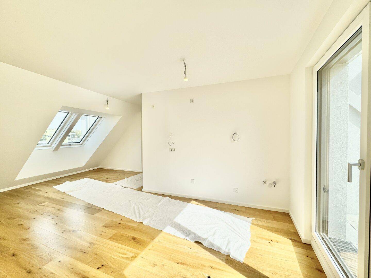 Unmöblierter Dachgeschossraum mit Holzboden und schrägen Dachfenstern, die viel Tageslicht hereinlassen.
