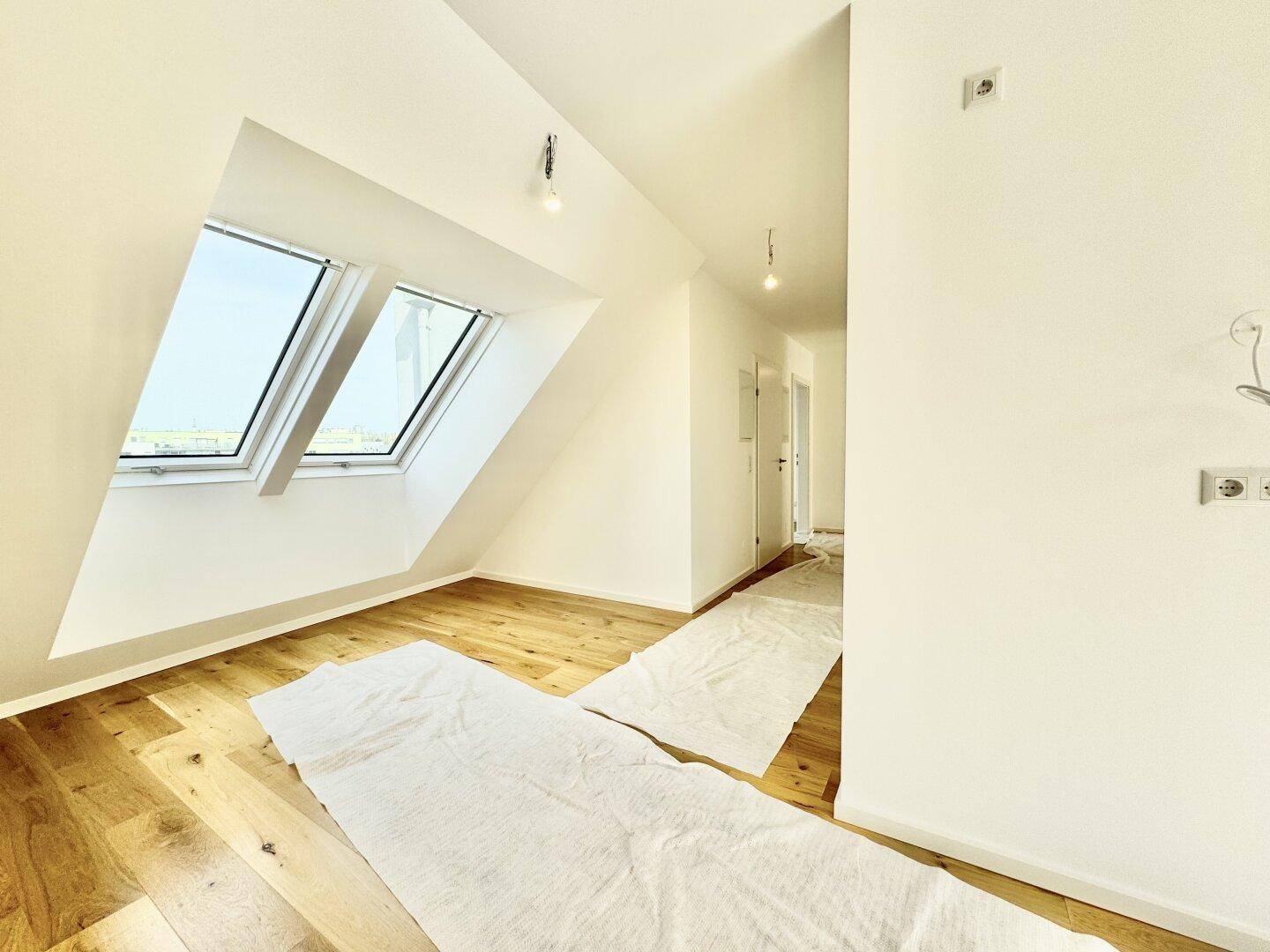 Heller Dachgeschossraum mit Holzboden und zwei großen Dachfenstern, die den Raum erhellen.