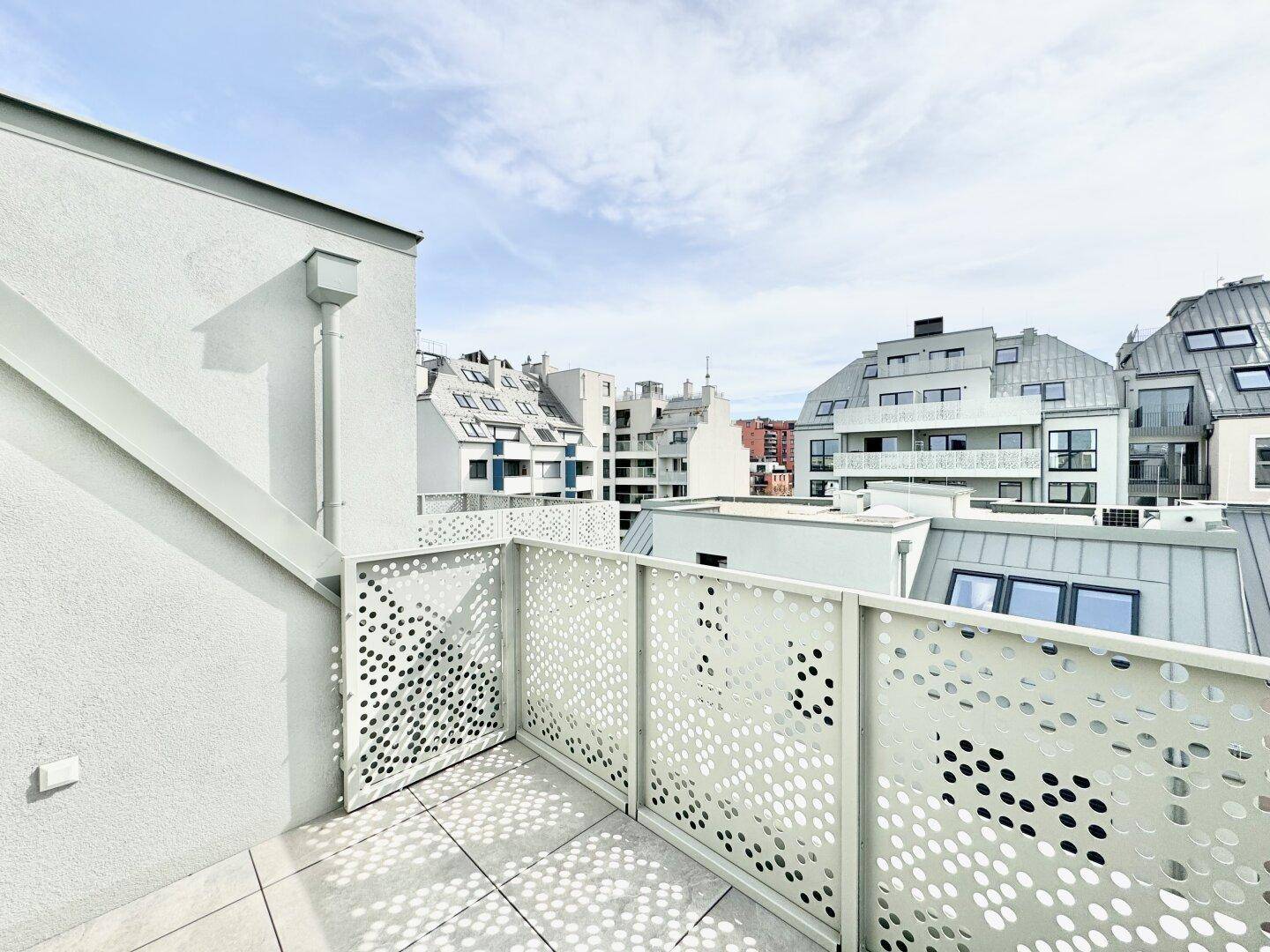 Moderne Dachterrasse mit perforiertem Geländer und Blick auf die umliegende Stadtbebauung.