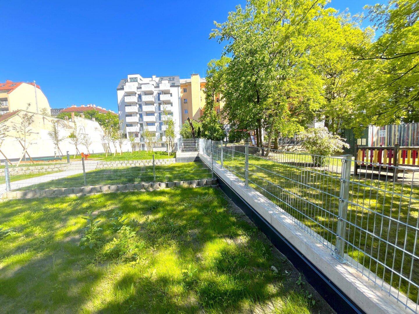 Gemeinschaftlicher Gartenbereich mit Rasen, Spielplatz und umzäunten Grünflächen.