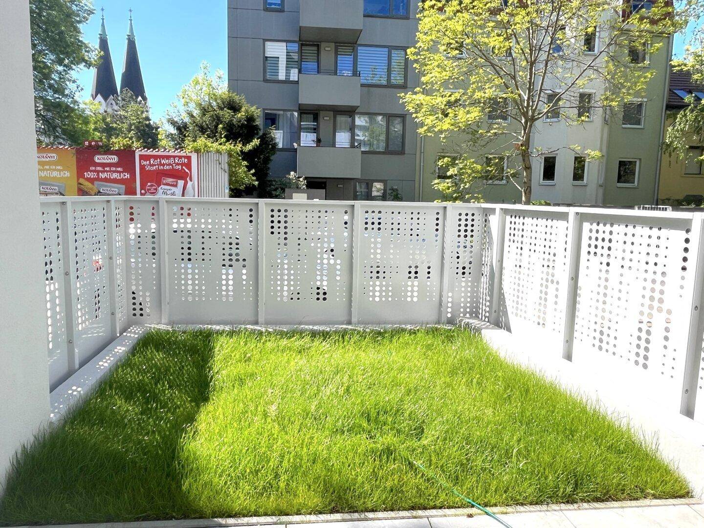 Gepflegter kleiner Garten mit Rasen und Terrasse, umgeben von einer modernen Zaunanlage.