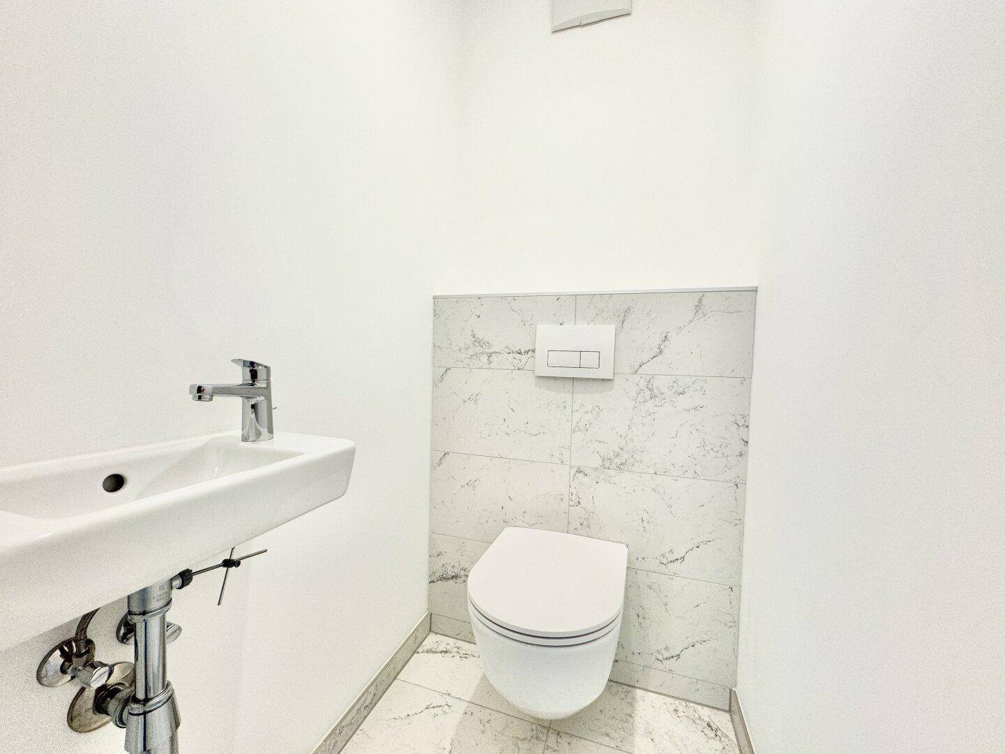 Kleines Gäste-WC mit wandhängendem WC und modernem Waschbecken in minimalistischem Design.
