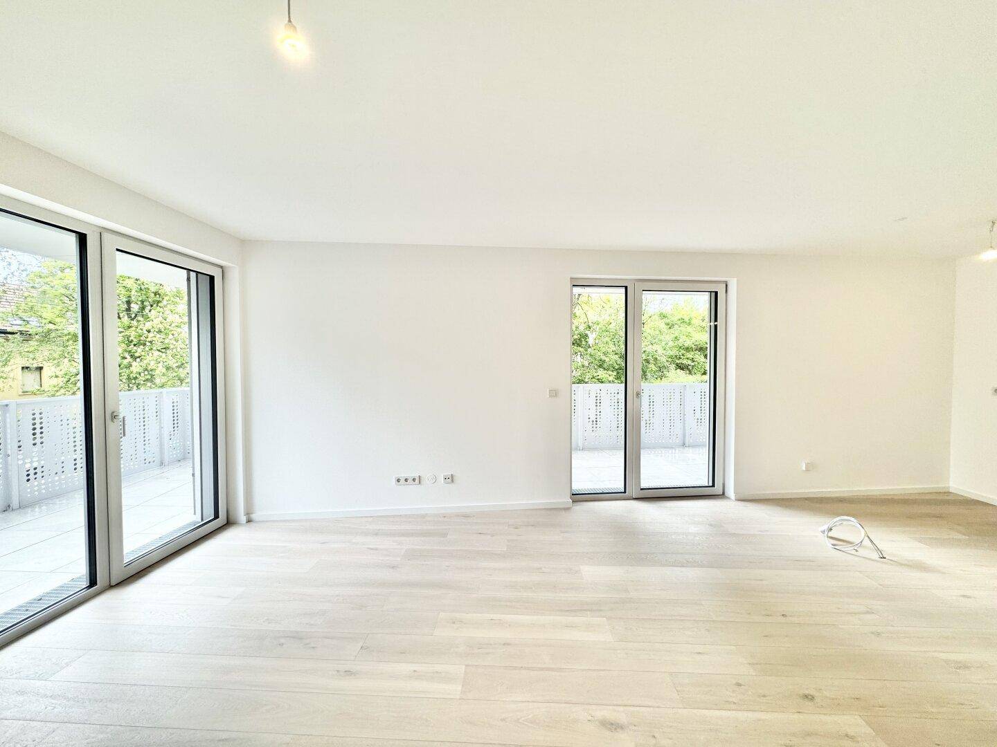 Heller, leerer Wohnraum mit großen Fenstern und direktem Zugang zu einem Balkon.