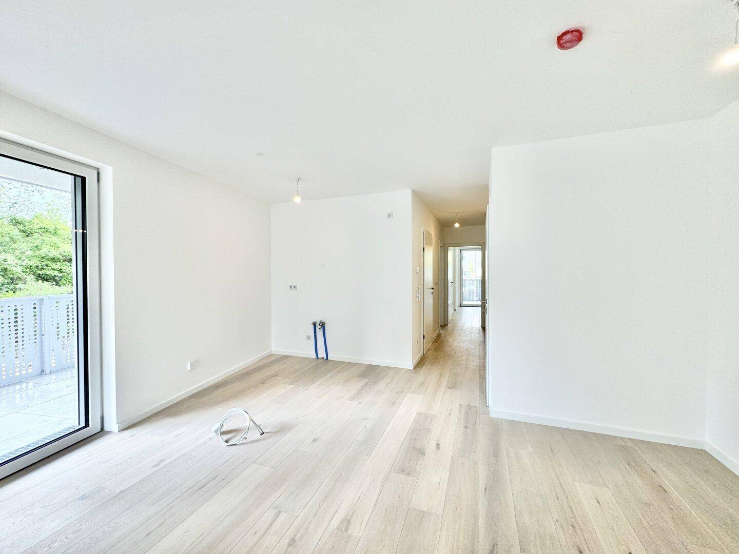 Heller Wohnbereich mit Zugang zum Balkon und einem Blick in den angrenzenden Flur.