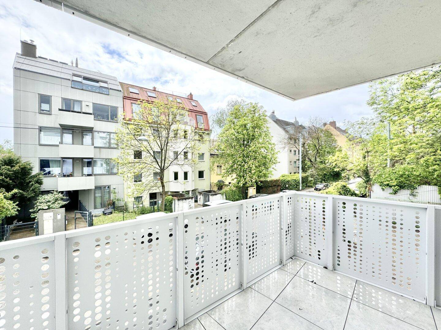Balkon mit moderner Brüstung und Ausblick auf die umliegenden Wohngebäude und Bäume.