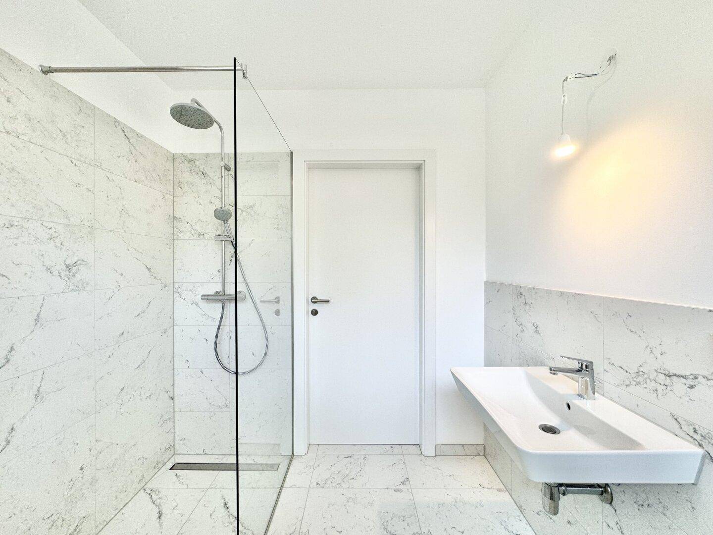 Modernes Badezimmer mit begehbarer Dusche, Glasabtrennung und eleganten Marmorfliesen.