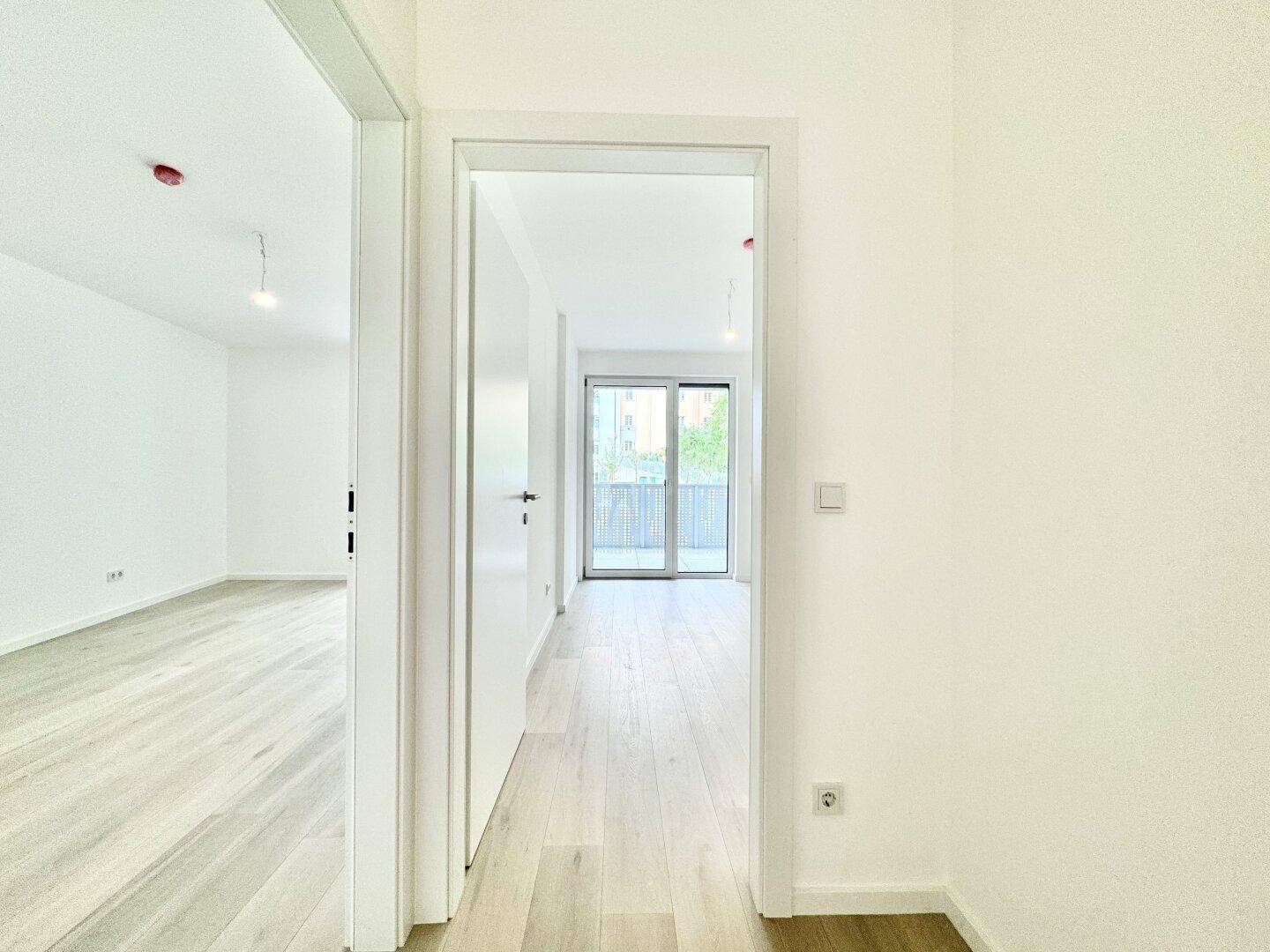 Heller Flur mit Blick in ein Zimmer, das Zugang zu einem Balkon bietet.