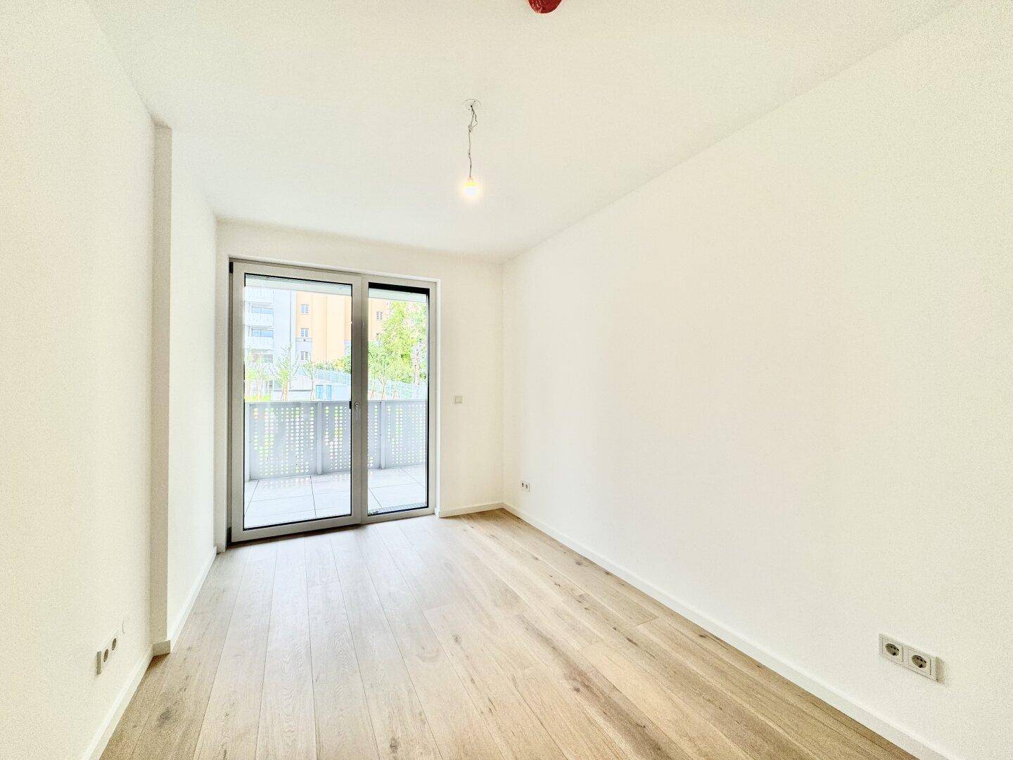 Unmöbliertes Schlafzimmer mit großen Fenstern und Zugang zum Außenbereich des Balkons.