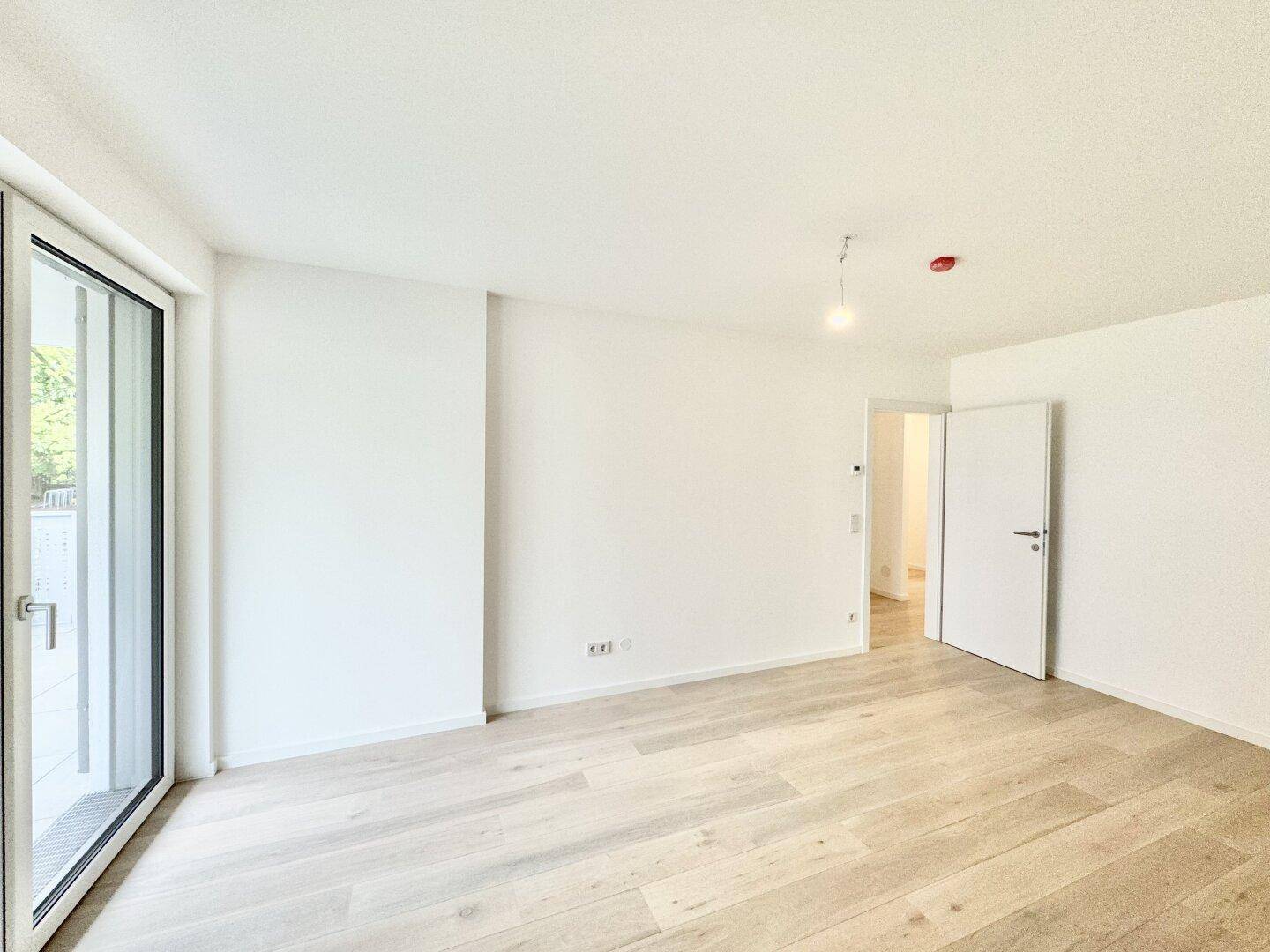 Helles Zimmer mit Holzboden, Balkonzugang und offener Tür zu einem weiteren Raum.