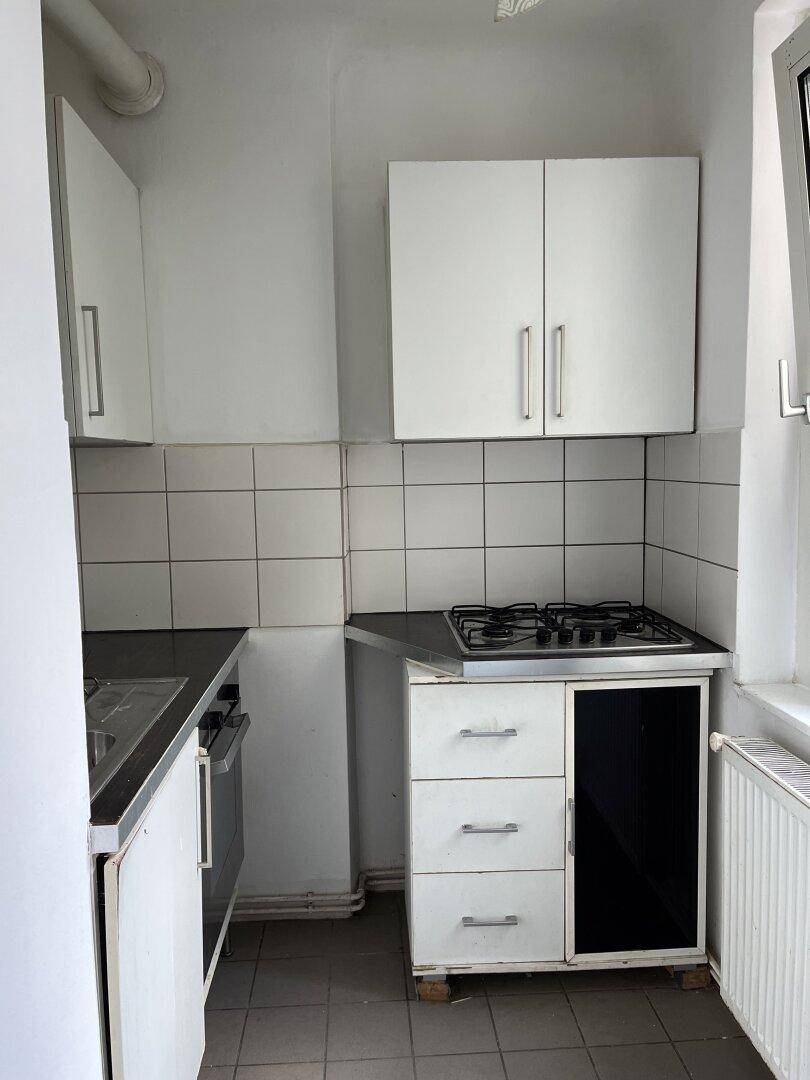 Kompakte Küche mit weißen Oberschränken, Gasherd und Fliesenboden, gut beleuchtet durch ein Fenster.