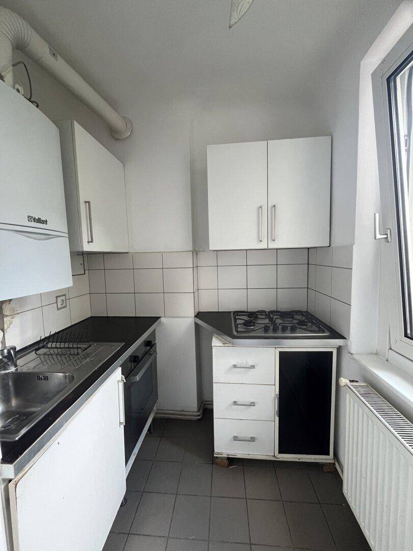 Funktionale Küche mit weißen Schränken, Gasherd, Backofen und Fenster.