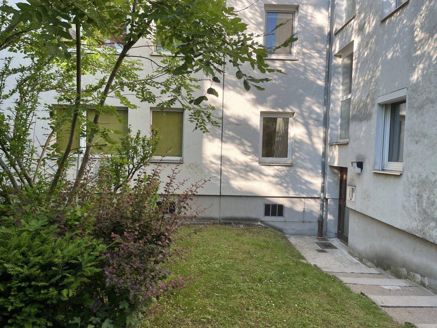 Gebäudefassade mit Fenstern und gepflegter Grünanlage, die das Haus umgibt.