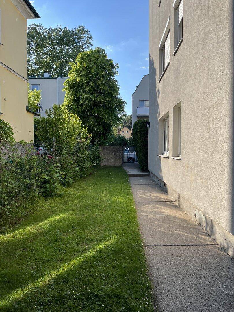 Seitenansicht eines Gebäudes mit schmalem Rasenstreifen und gepflastertem Weg.