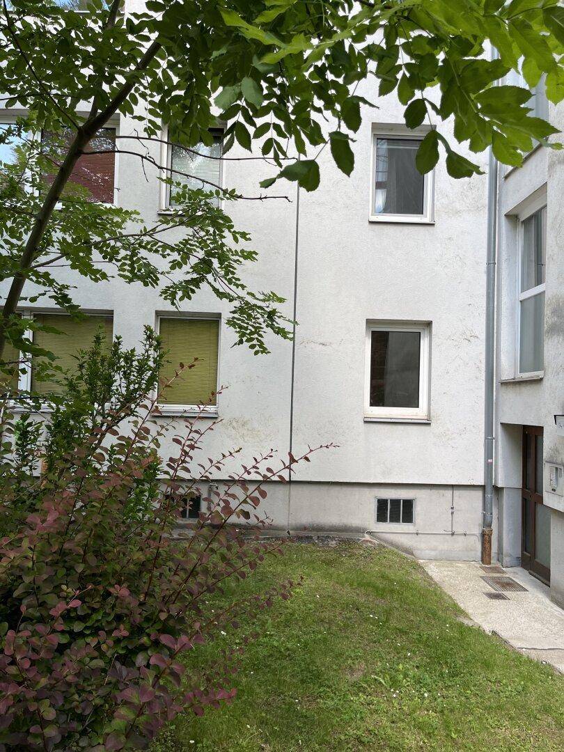Fassade eines Wohngebäudes mit mehreren Fenstern und umliegender Grünfläche.