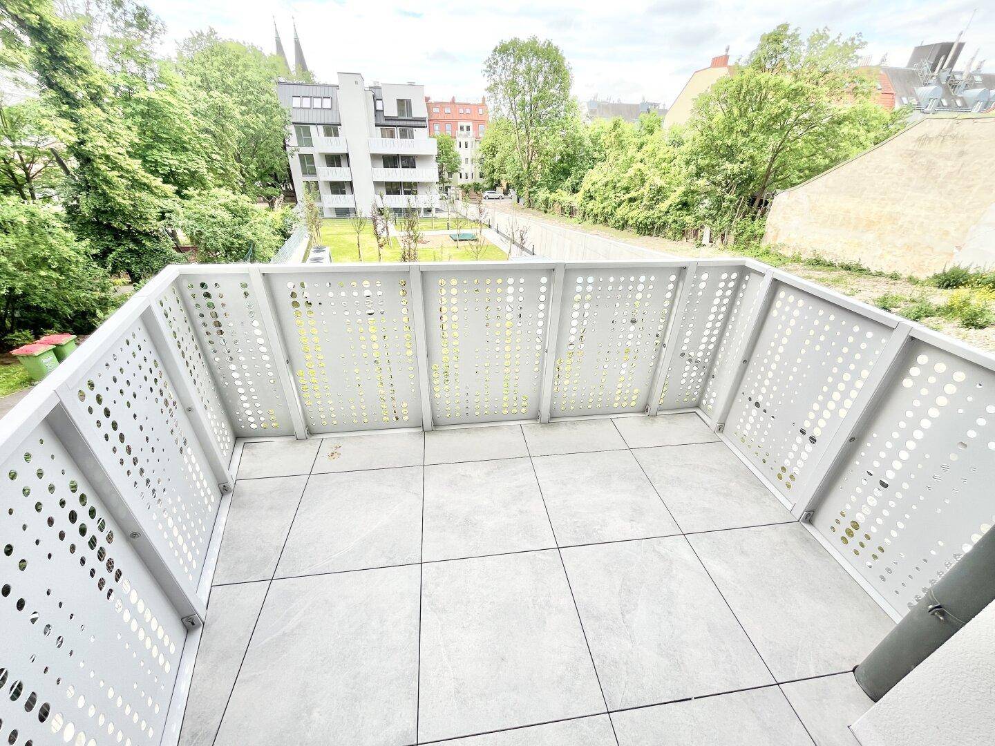 Geräumiger Balkon mit Fliesenboden und modernem Geländer, bietet einen weiten Ausblick ins Grüne.