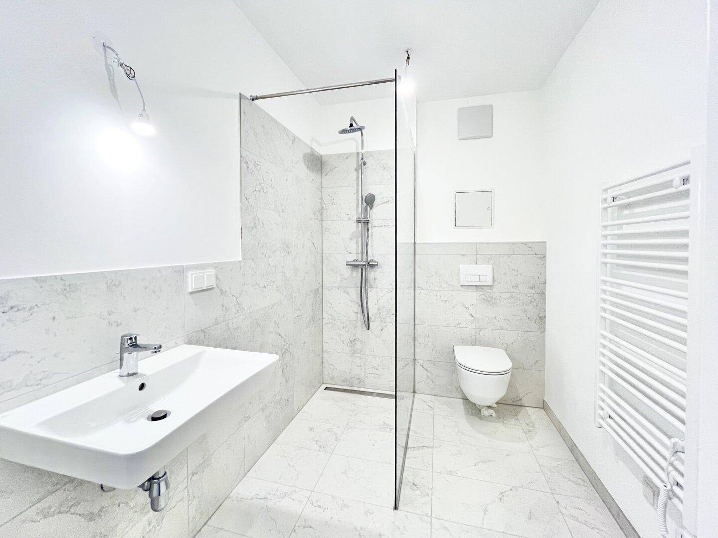 Modernes Badezimmer mit begehbarer Dusche, Wand-WC und beheiztem Handtuchhalter, elegant gefliest.