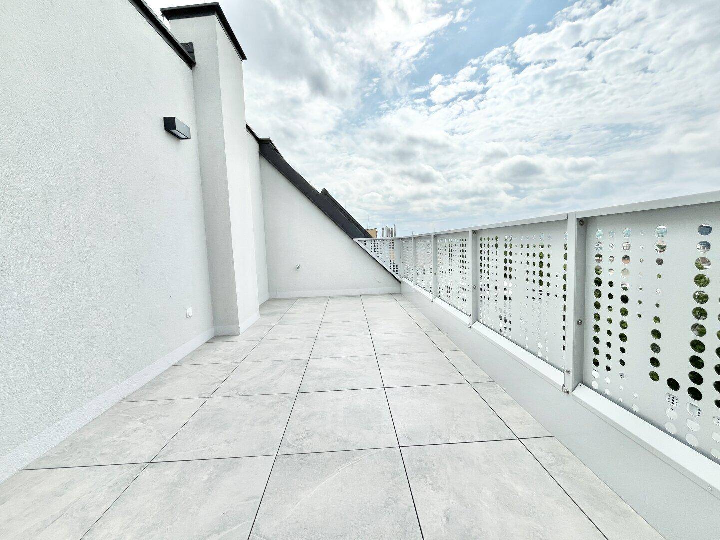 Große, helle Dachterrasse mit modernen Fliesen und weißer Brüstung unter bewölktem Himmel.