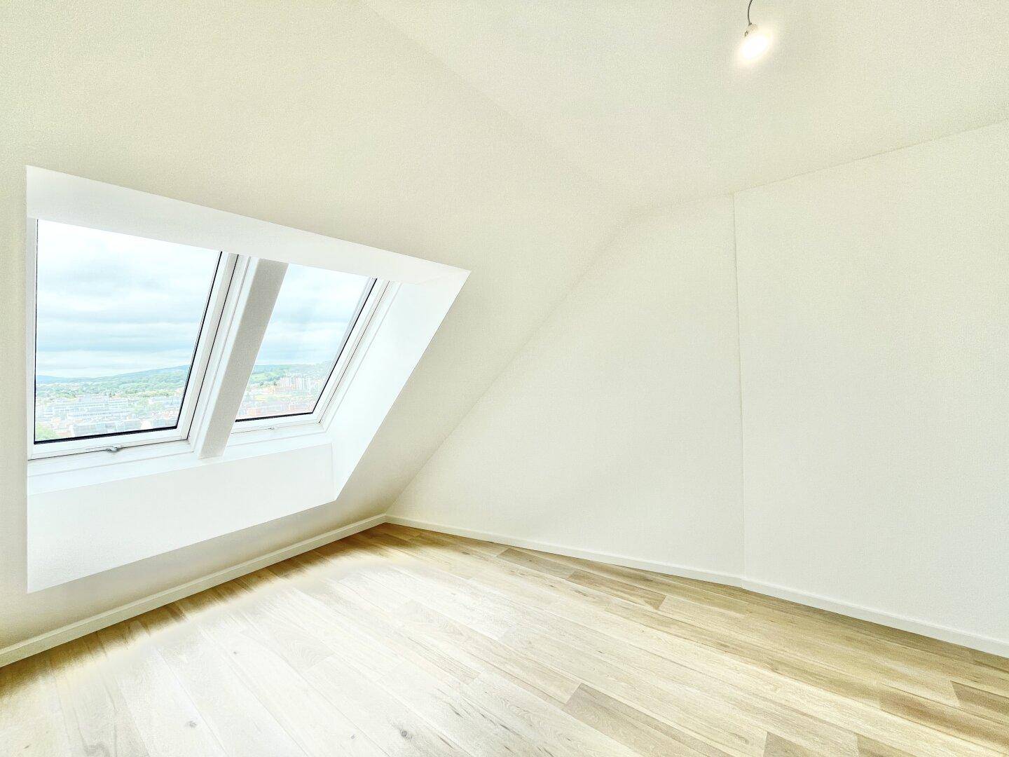Heller Raum mit Holzboden und großem Dachfenster, ideal für ein Schlafzimmer oder Büro.