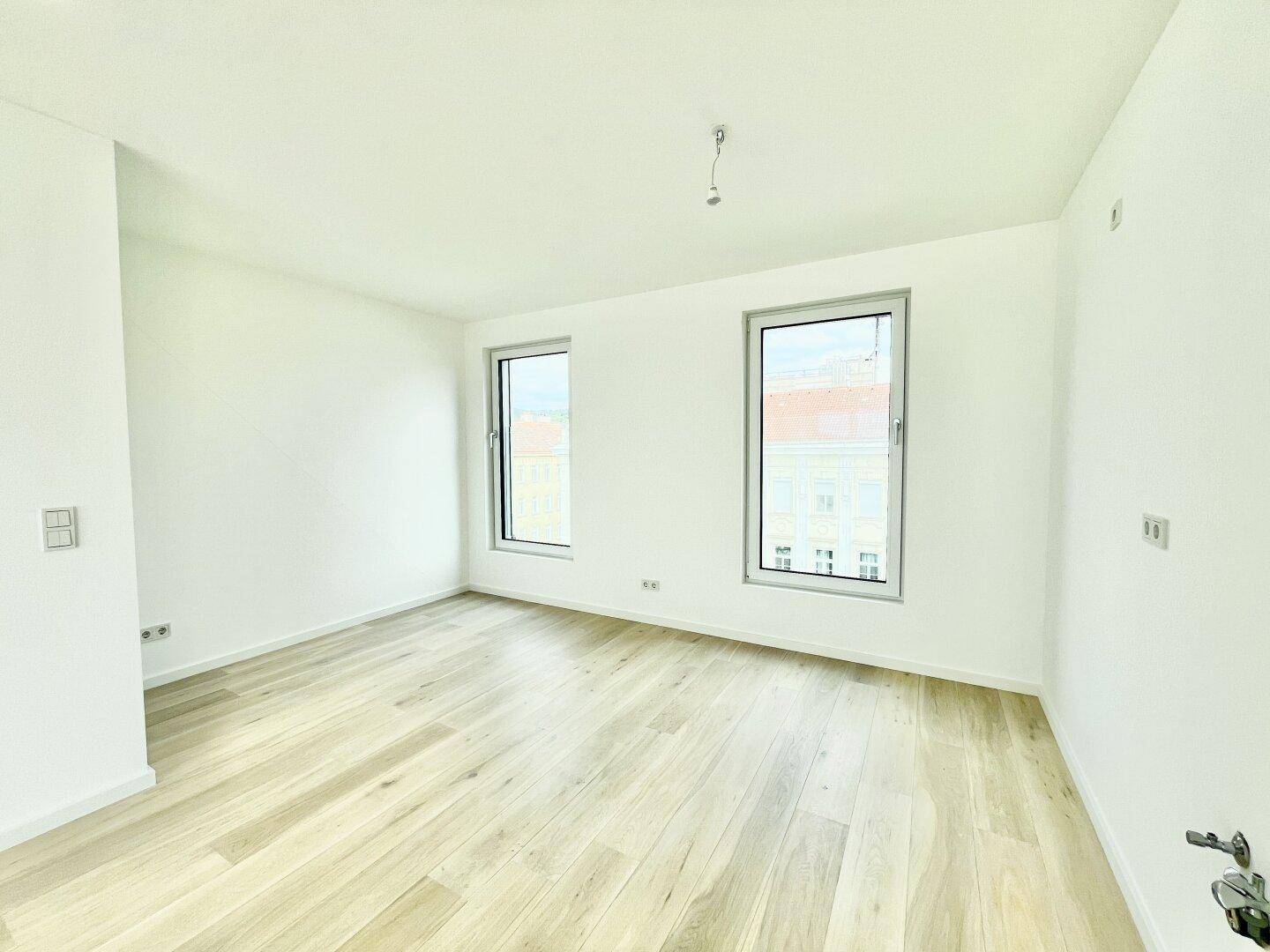 Heller, leerer Raum mit modernem Holzboden und zwei Fenstern, bereit zur individuellen Gestaltung.