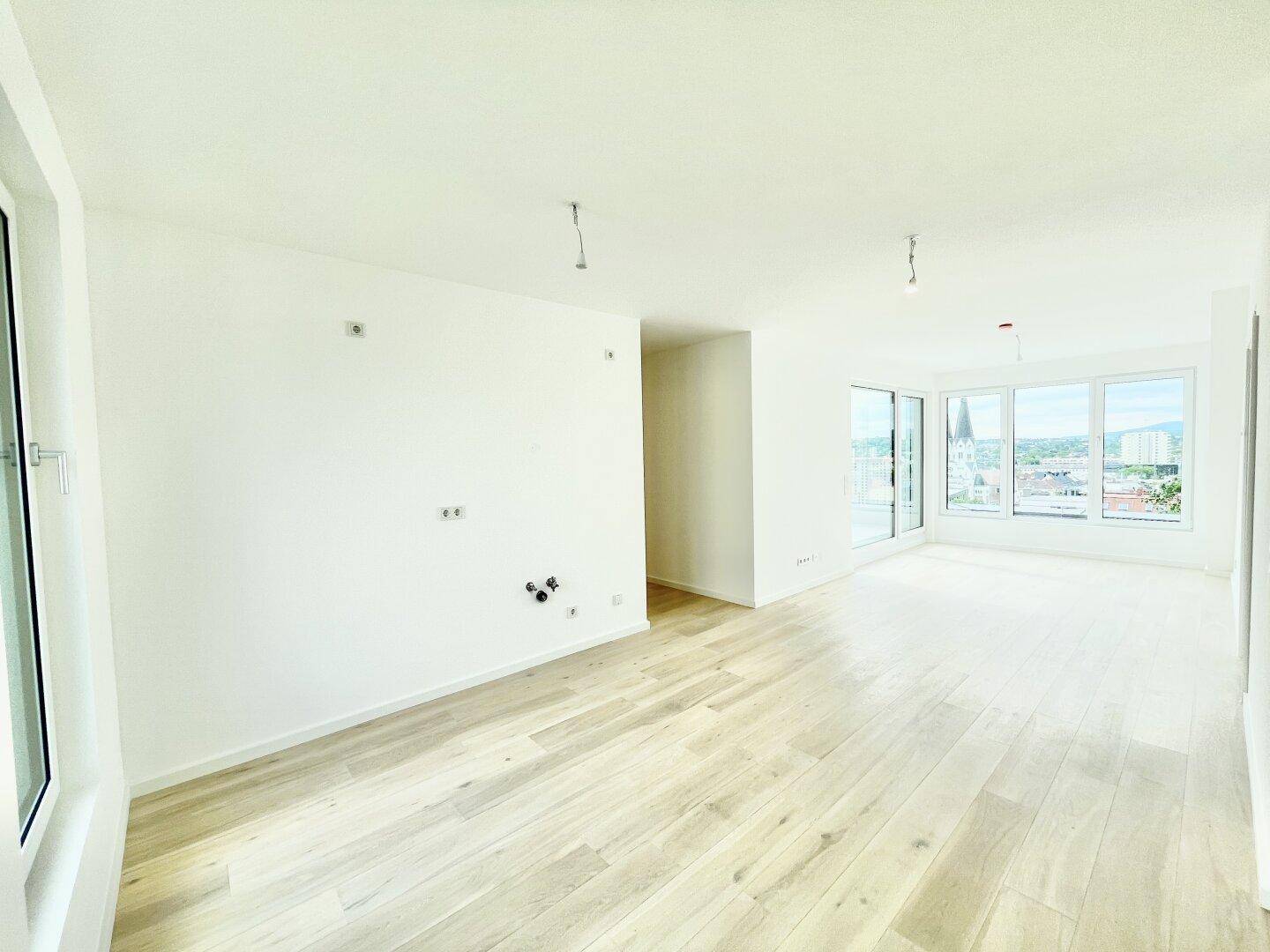 Geräumiger, heller Raum mit Holzboden und großen Fenstern, bietet Potenzial für Wohn- oder Essbereich.