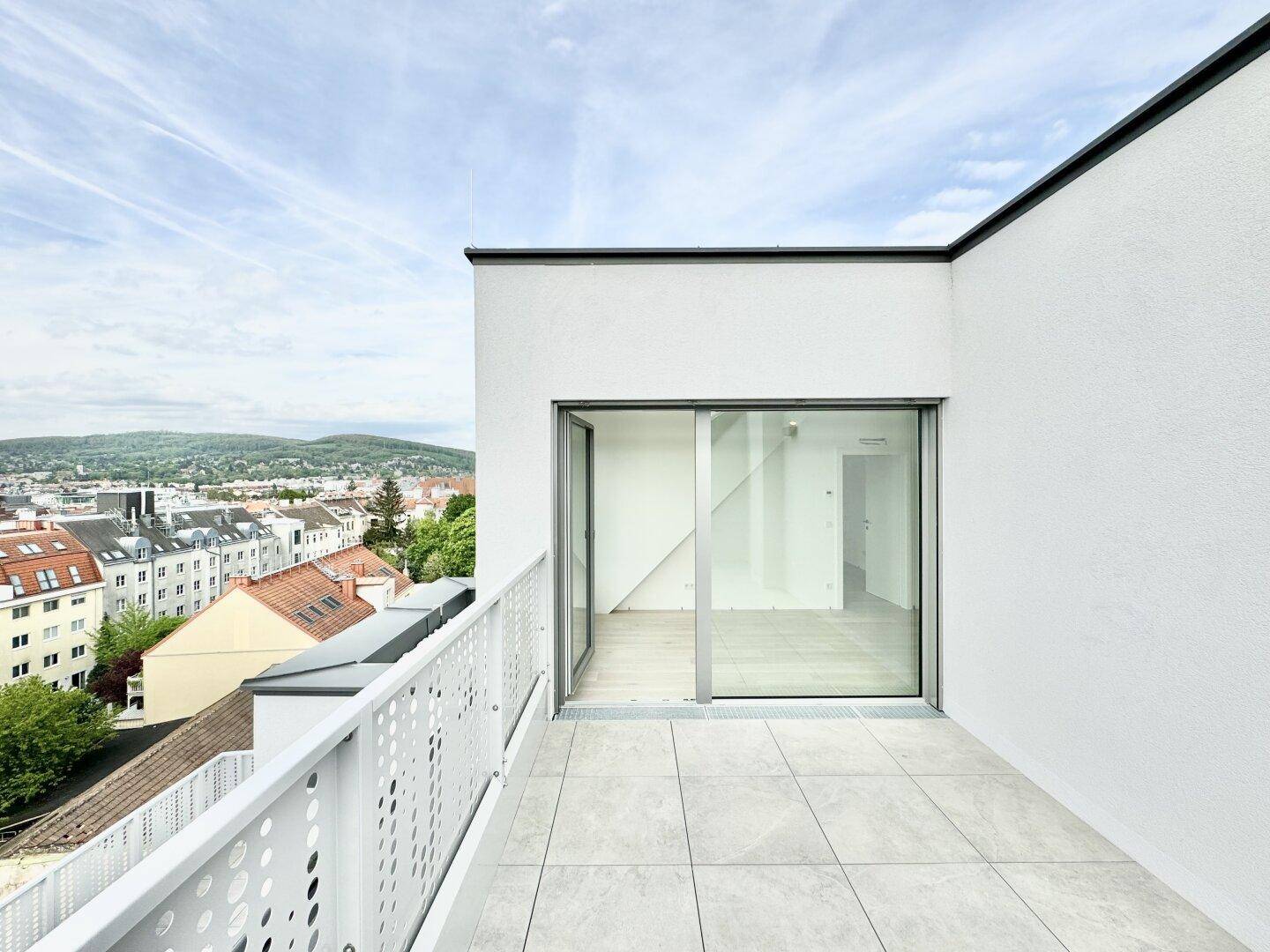 Moderne Terrasse mit Fliesenboden, Glasfront und weitem Blick über die Stadt und grüne Hügel.