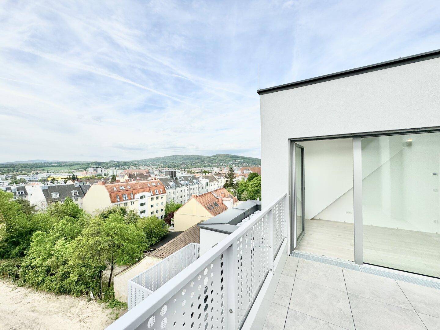 Helle Terrasse mit Fliesen und moderner Brüstung, bietet einen weiten Blick über die Stadt und Natur.