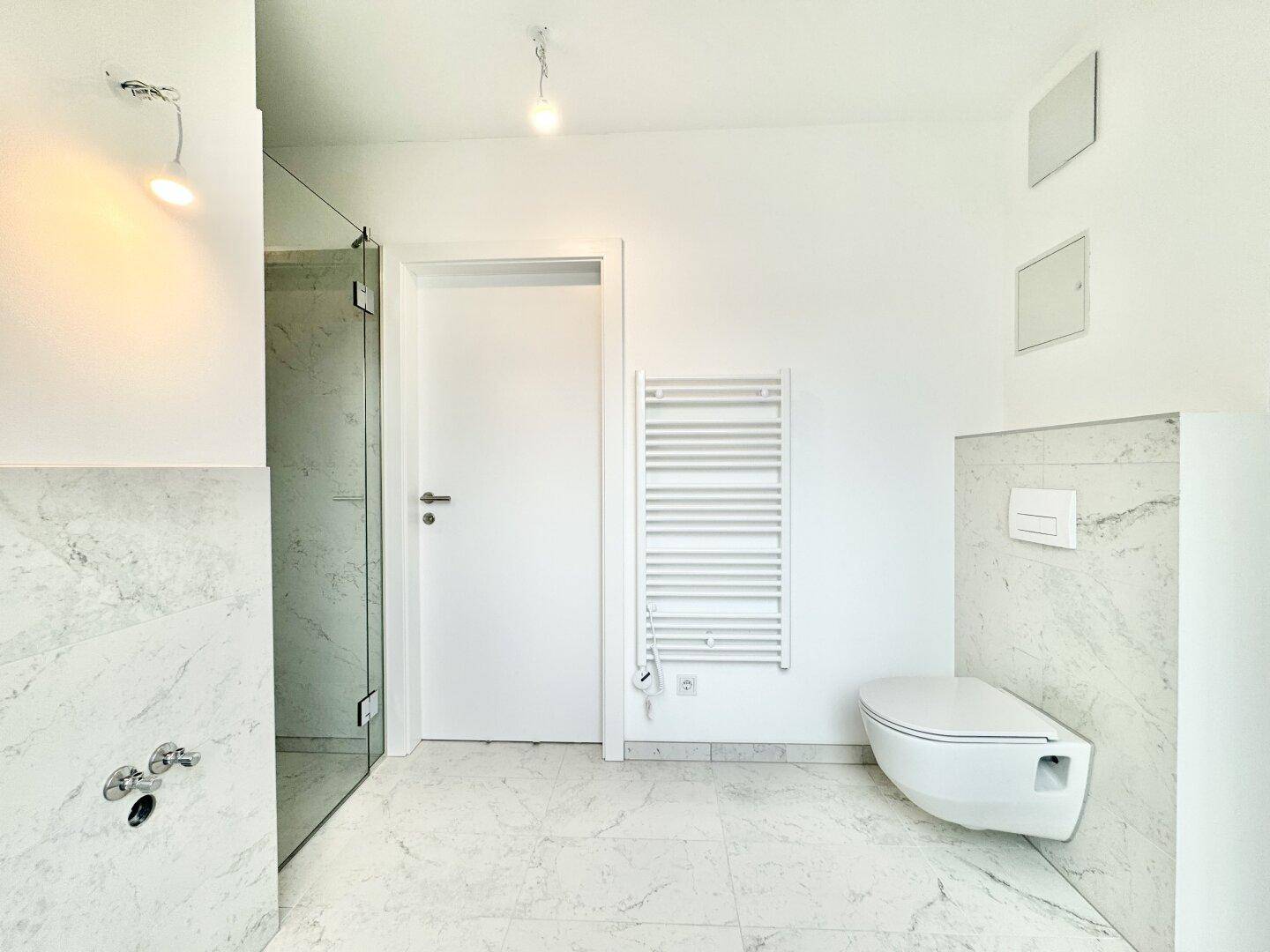Modernes Badezimmer mit Marmorfliesen, begehbarer Dusche, wandhängendem WC und Handtuchheizkörper.