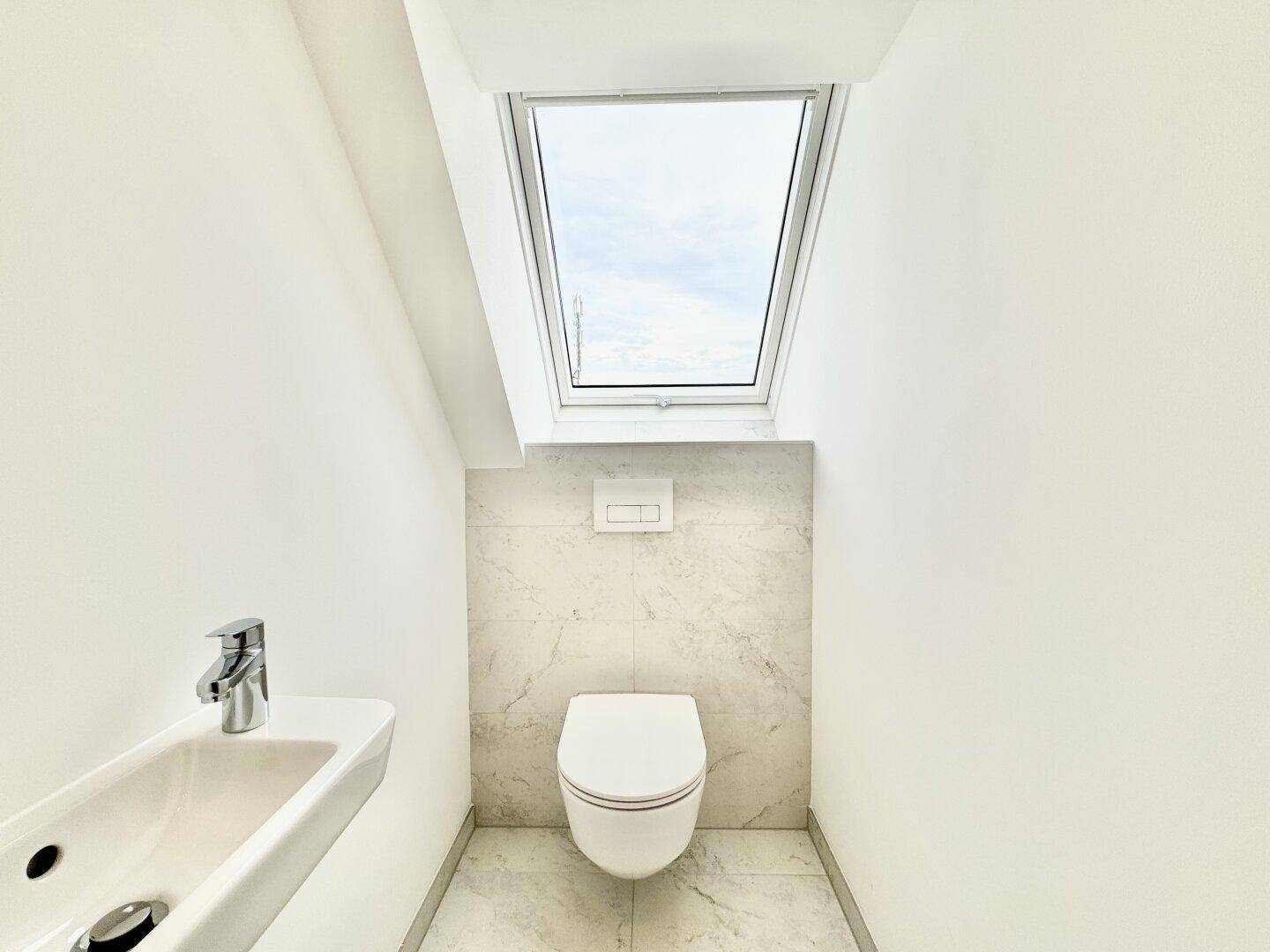 Helles Gäste-WC mit wandhängendem WC, kleinem Waschbecken und Dachfenster unter Schräge.
