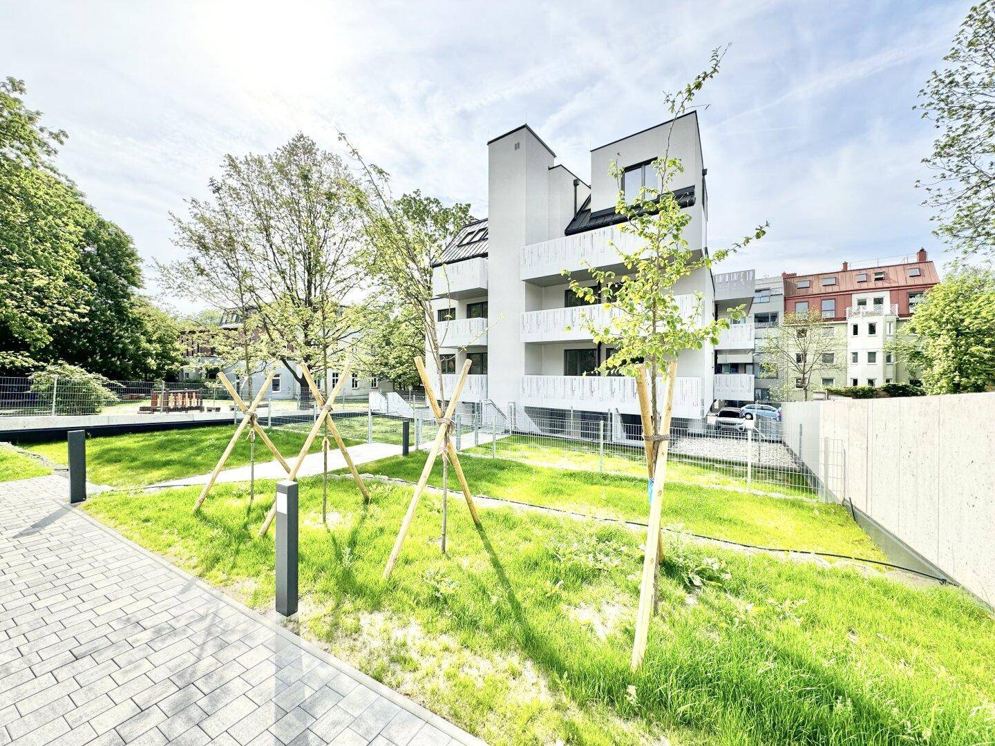 Moderne Wohnanlage mit weißer Fassade, Balkonen und neu angelegtem Gartenbereich mit jungen Bäumen.