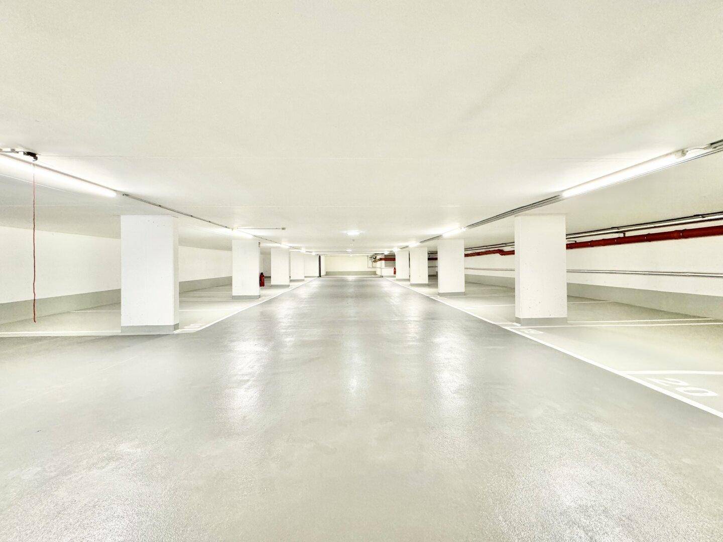 Geräumige Tiefgarage mit vielen Stellplätzen, hellen Säulen und sauberem Betonboden.
