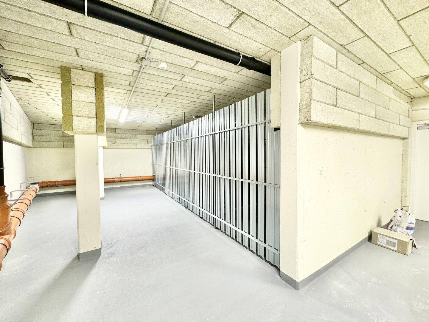 Kellerabteil mit individuellen Lagerboxen, Betonboden und sichtbaren Installationen.