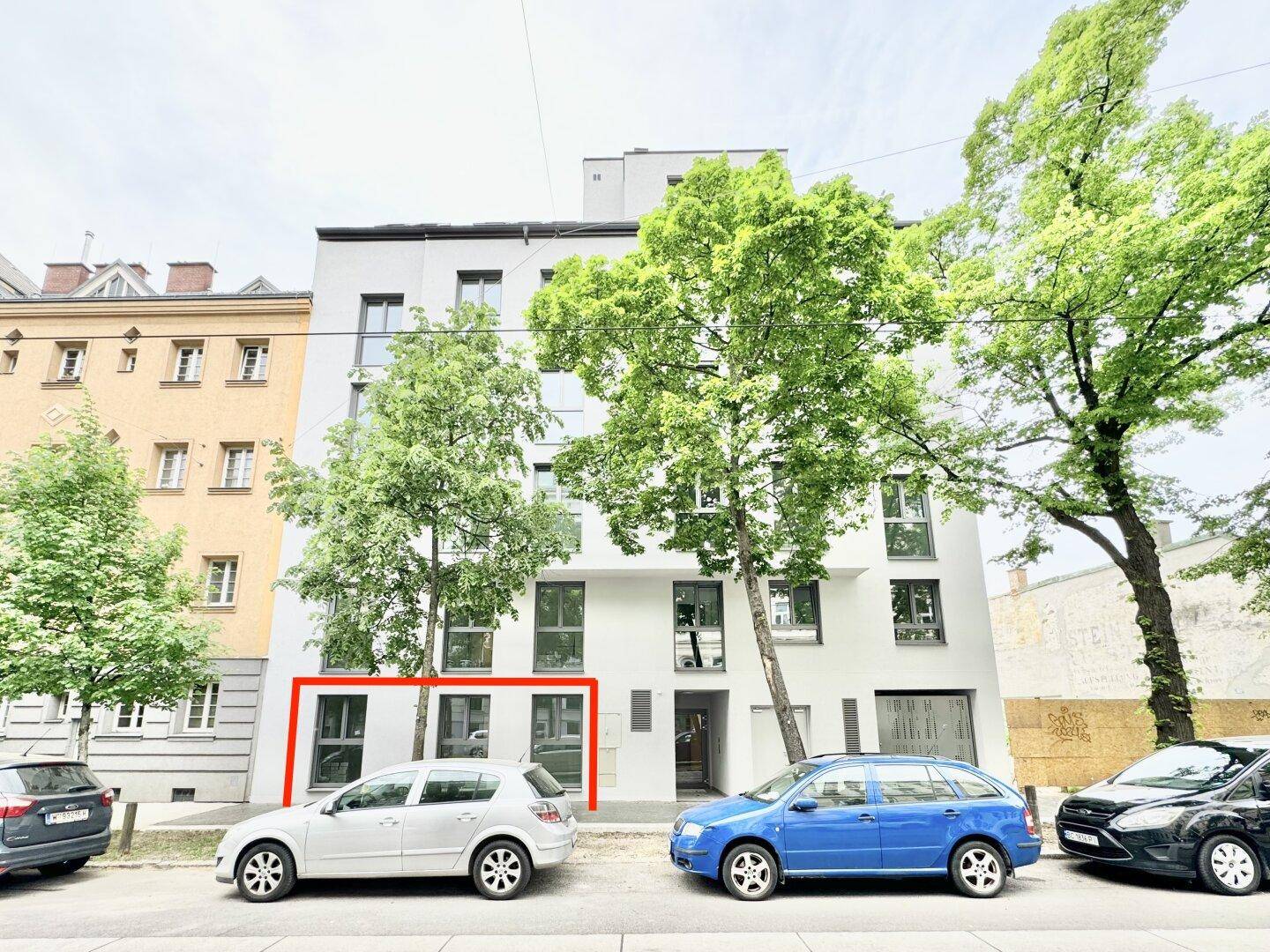 Gesamtansicht der modernen Gebäudefassade von der gegenüberliegenden Straßenseite mit Bäumen und Autos.