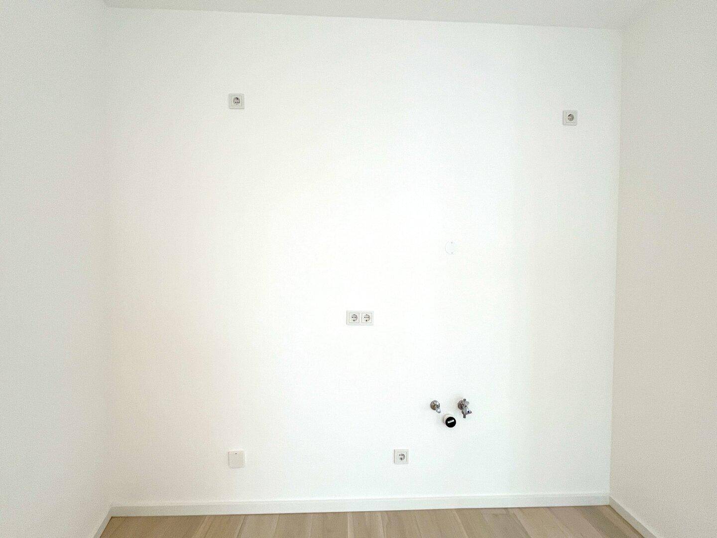 Weiße Wand mit Steckdosen und Wasseranschlüssen, vorbereitet für eine moderne Küche oder einen Hauswirtschaftsraum.