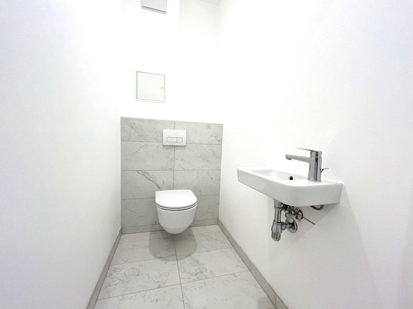Modernes Gäste-WC mit wandhängender Toilette, kleinem Waschbecken und hellen Fliesen.