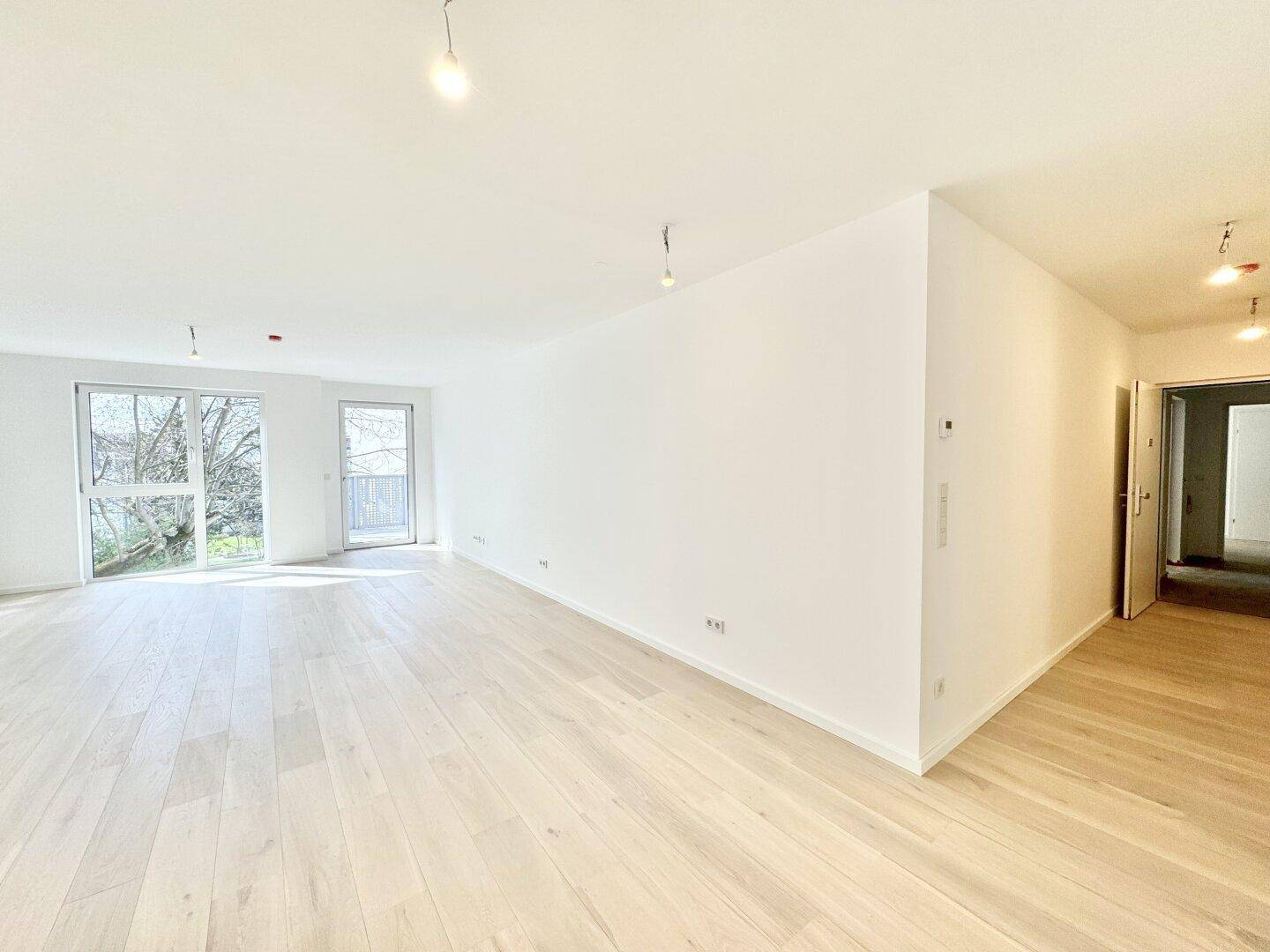 Großzügiger, heller Wohnbereich mit Holzboden und Zugang zum Außenbereich, ideal für offenes Wohnen.