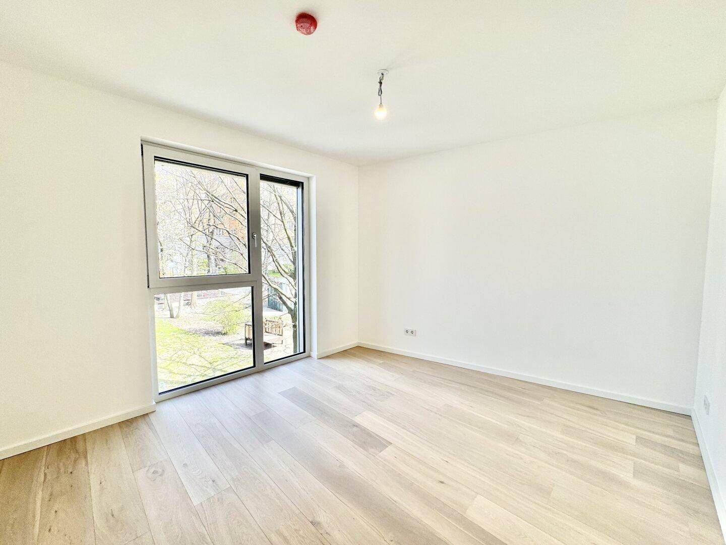 Heller Raum mit Holzboden und großen Fenstern, bietet viel Tageslicht und Blick ins Grüne.
