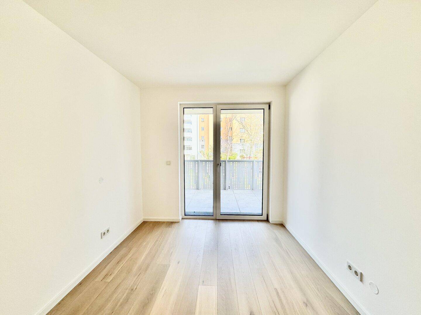 Heller Raum mit Holzboden und Balkonzugang, bietet viel Tageslicht und eine offene Atmosphäre.
