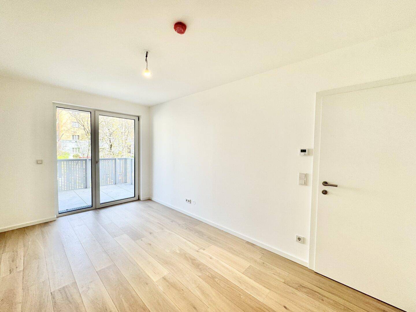 Heller Raum mit Holzboden und Zugang zu einem Balkon, bietet viel Tageslicht.