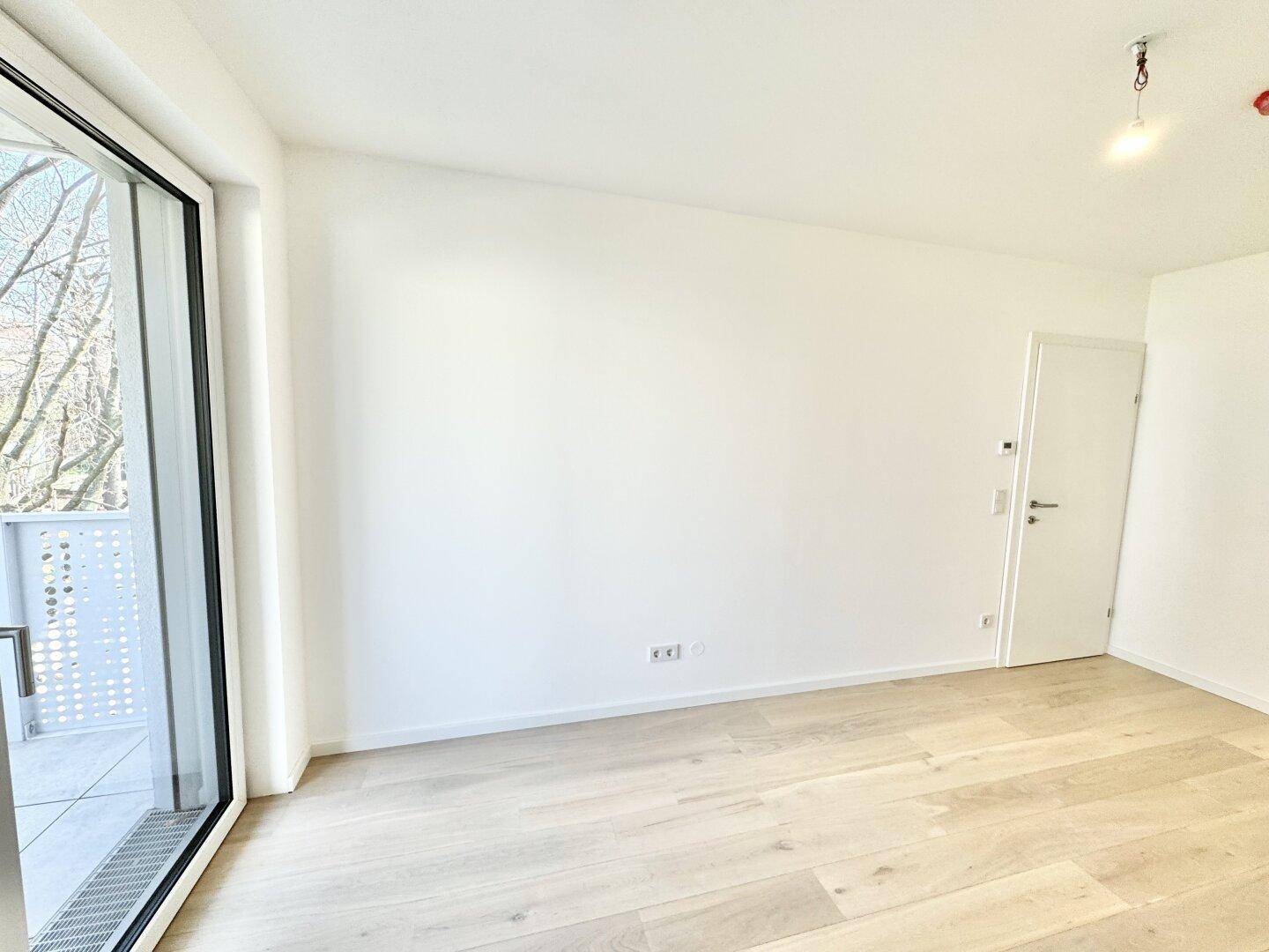 Heller Raum mit Holzboden und Zugang zu einem Balkon, bietet viel Tageslicht.