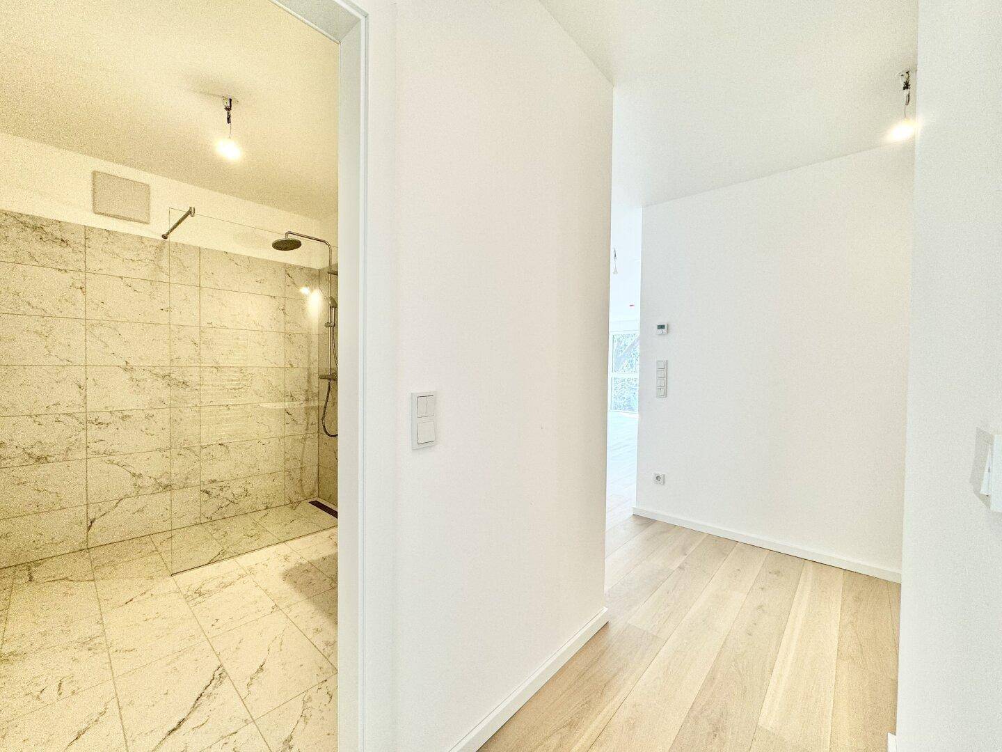 Heller Flur mit Holzboden, der zu einem modernen Badezimmer mit Marmorfliesen führt.