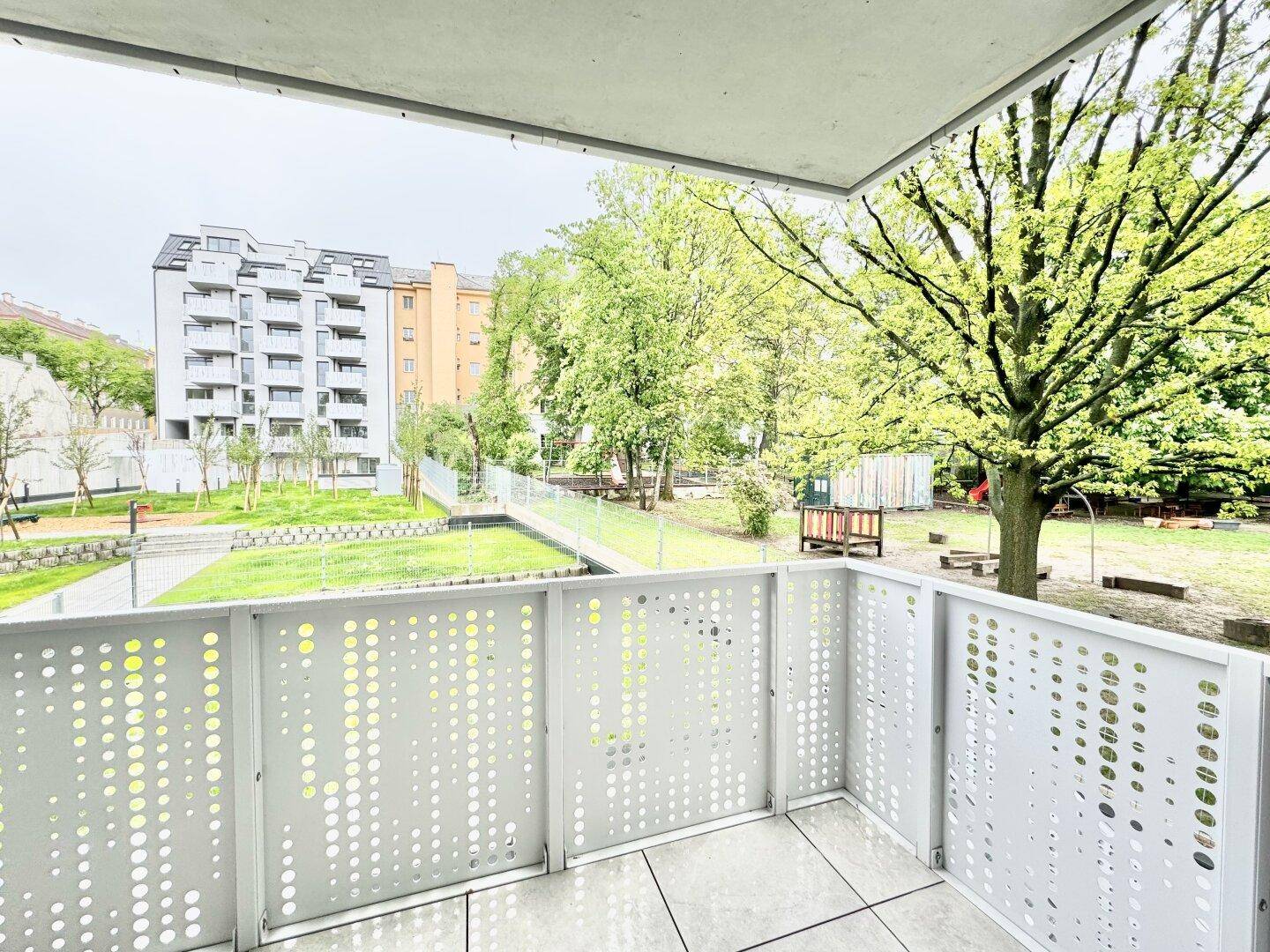 Balkon mit Blick auf einen grünen Innenhof und einen Spielplatz, umgeben von Bäumen.