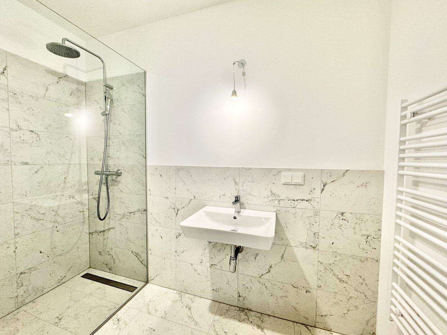 Modernes Badezimmer mit großer begehbarer Dusche, Marmorfliesen und beheiztem Handtuchhalter.
