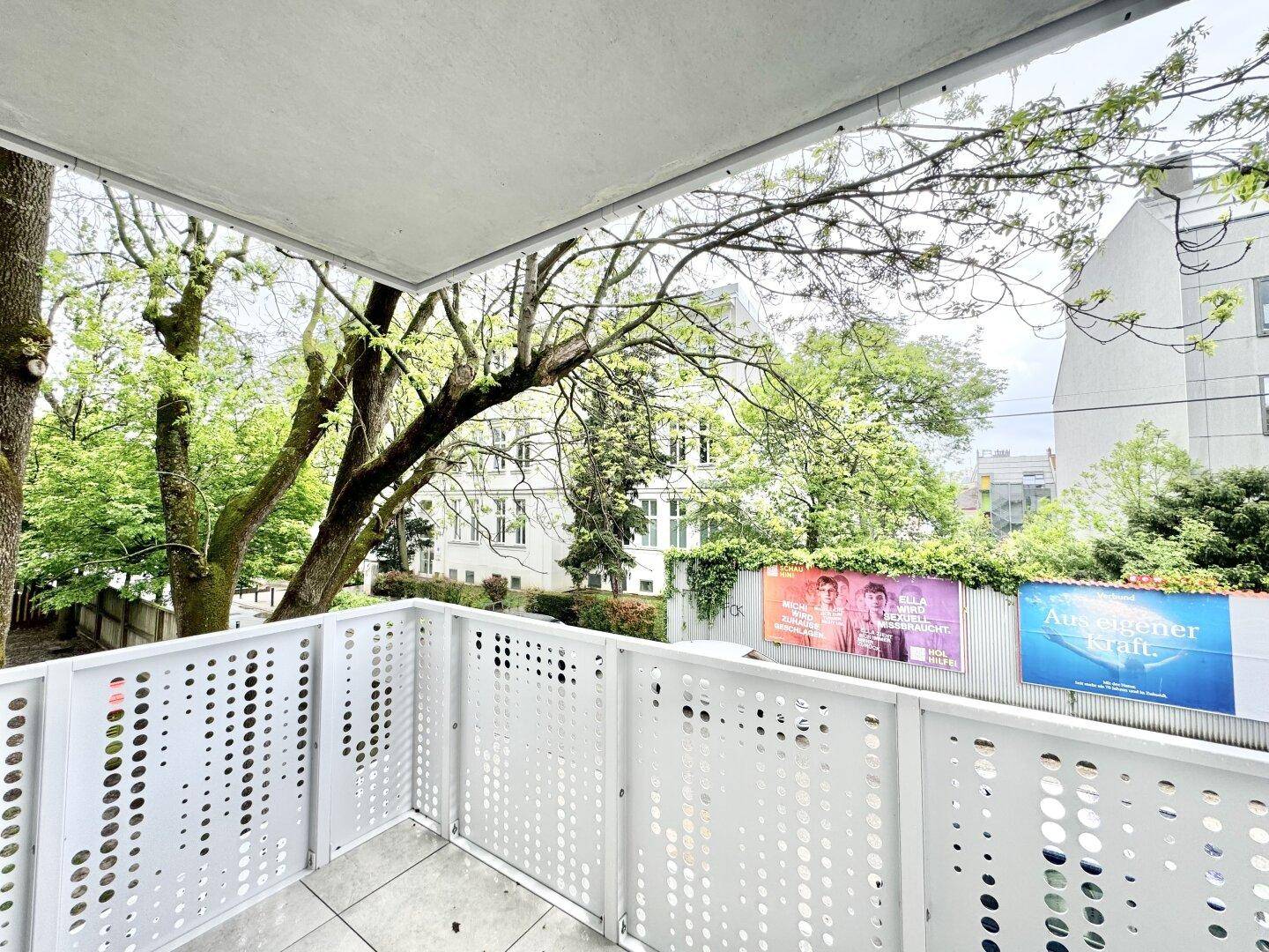 Moderner Balkon mit perforiertem Geländer und Blick auf Bäume und die Umgebung.