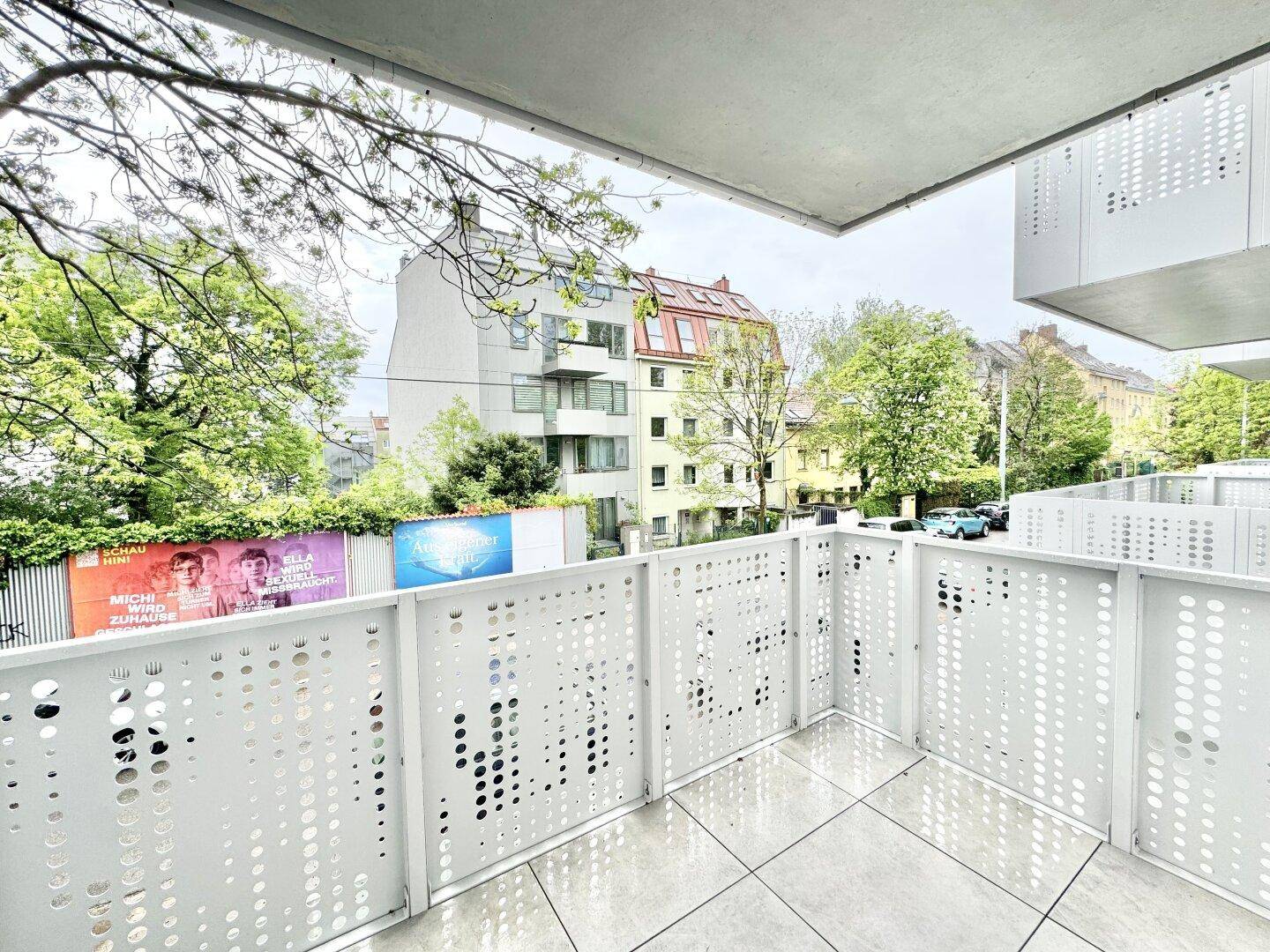 Moderner Balkon mit perforiertem Geländer und Blick auf die umliegende Wohngegend und Bäume.