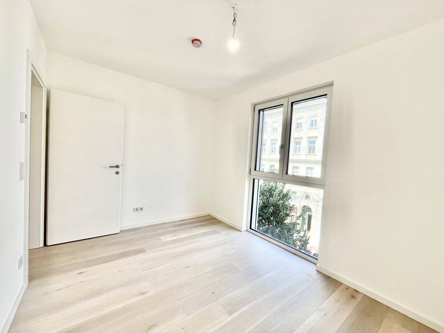 Leerer Raum mit Holzboden, weiß gestrichenen Wänden und einem großen Fenster für viel Licht.